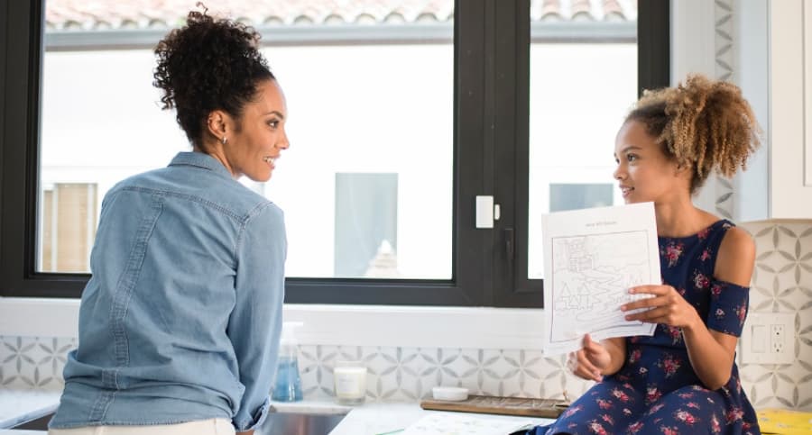 Mother and daughter in front of a kitchen window with an ADT home security sensor